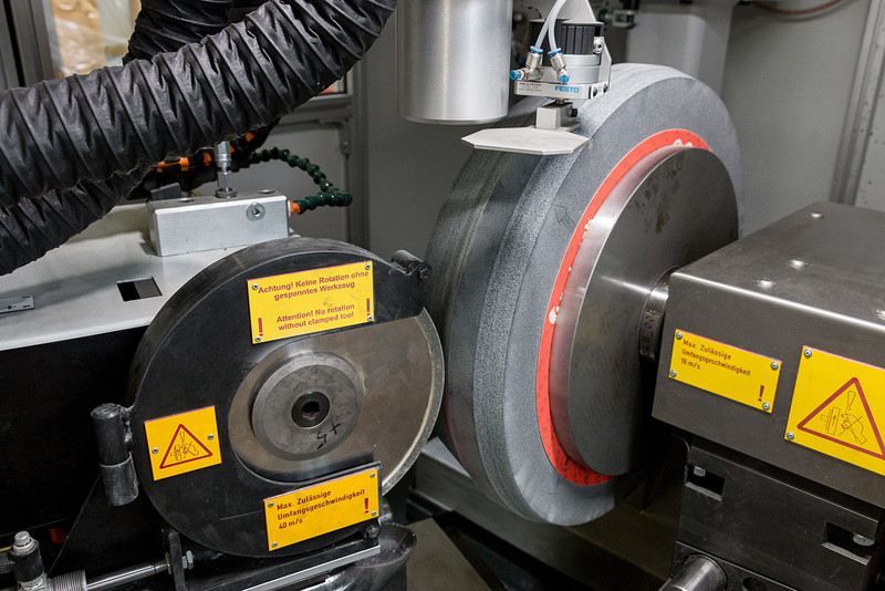 View of the AP900 - right, the large grinding wheel to be dressed - left, the silicon disk that precisely performs the dressing and profiling work on the grinding wheel. The profile that is being abraded by the silicon wheel can already be clearly recognized on the large grinding wheel. View of the AP900 - right, the large grinding wheel to be dressed - left, the silicon disk that precisely performs the dressing and profiling work on the grinding wheel. The profile that is being abraded by the silicon wheel can already be clearly recogni