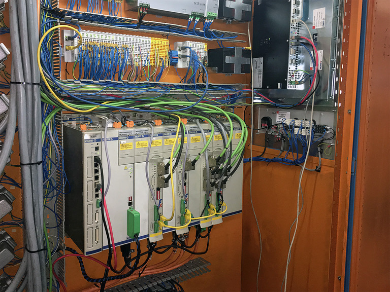 Vista interna dell’armadio elettrico: un Flexium NCK (a sinistra), azionamenti assi con safety, schede I/O con moduli I/O di sicurezza e il retro dei pannelli FS192i e MP05 (sulla destra).